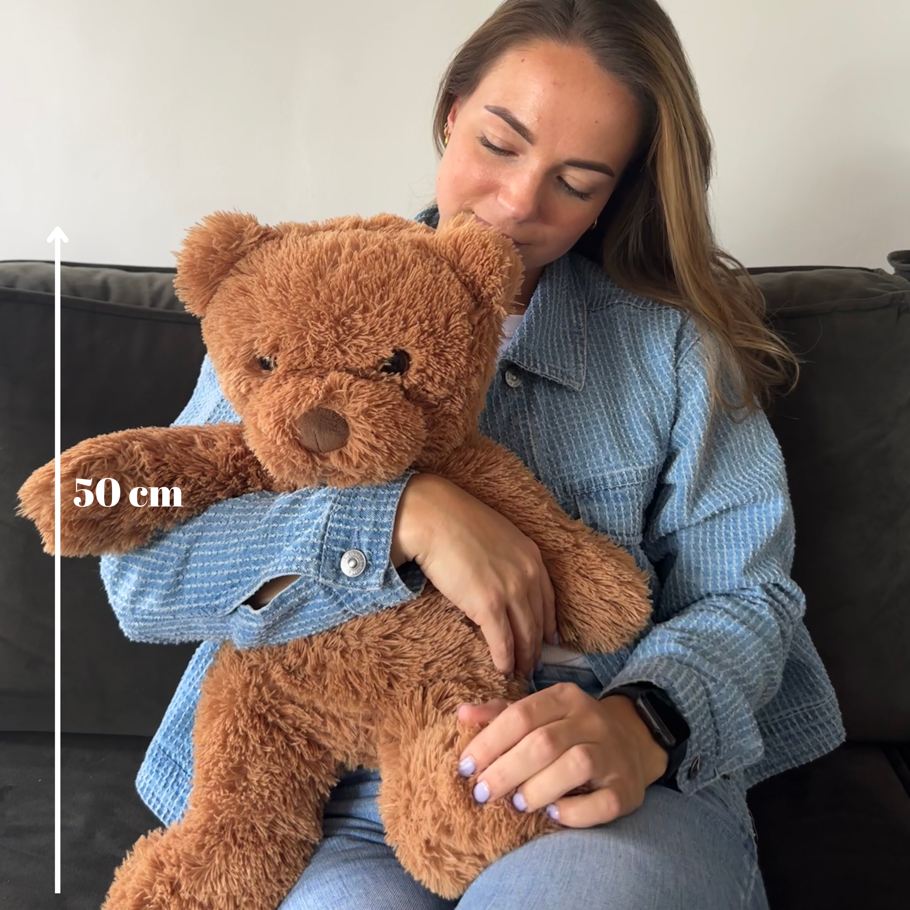 Vrouw die de bruine verzwaringsknuffel beer vasthoudt met een witte pijl die de lengte van 50 cm aangeeft.