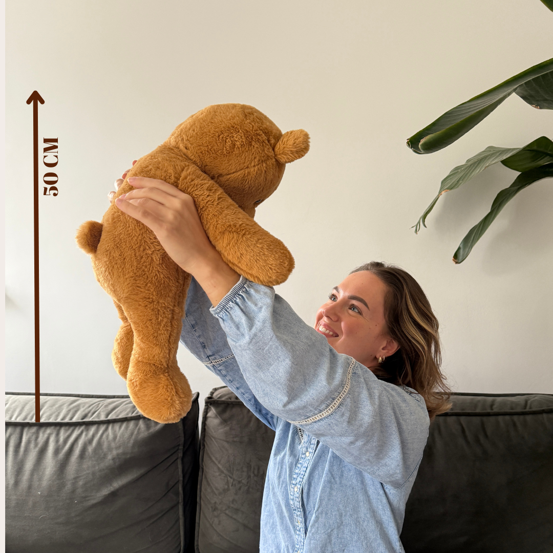 De verzwaringsknuffel beer (50 cm) omhoog gehouden om de grootte en het volume voor volwassenen en kinderen te tonen.