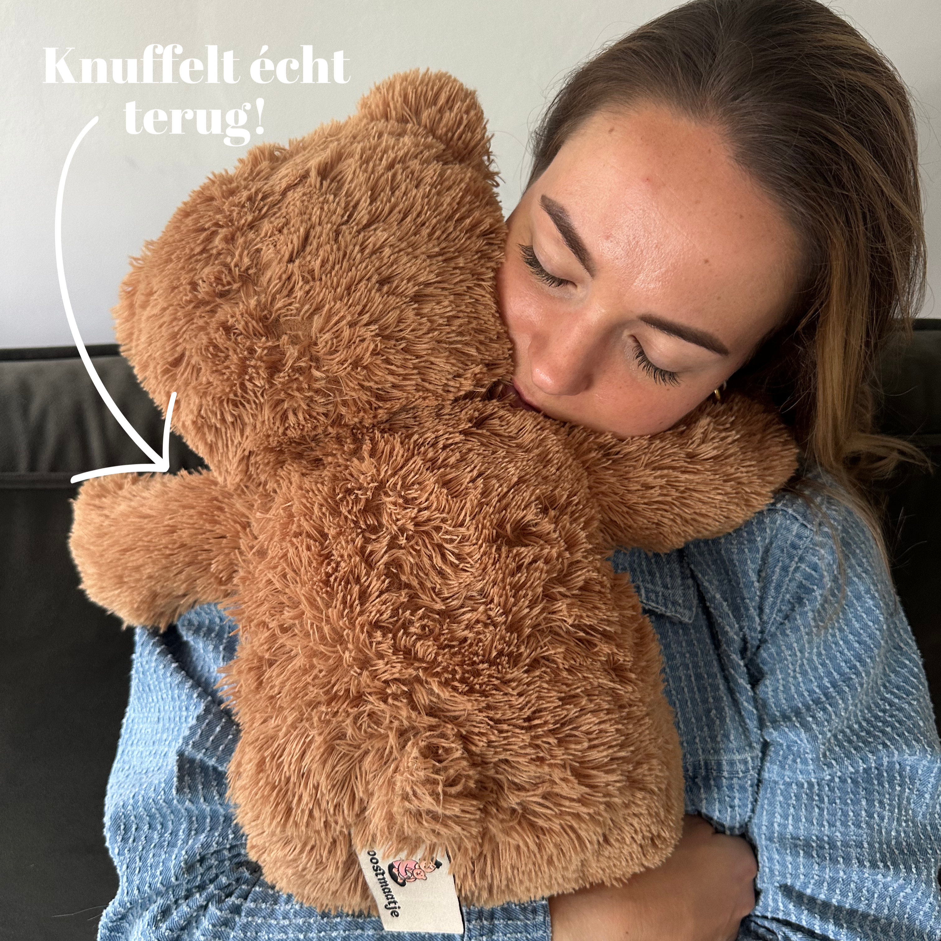 Close-up van een vrouw die de zachte bruine beer stevig vasthoudt met de tekst 'Knuffelt écht terug!'.