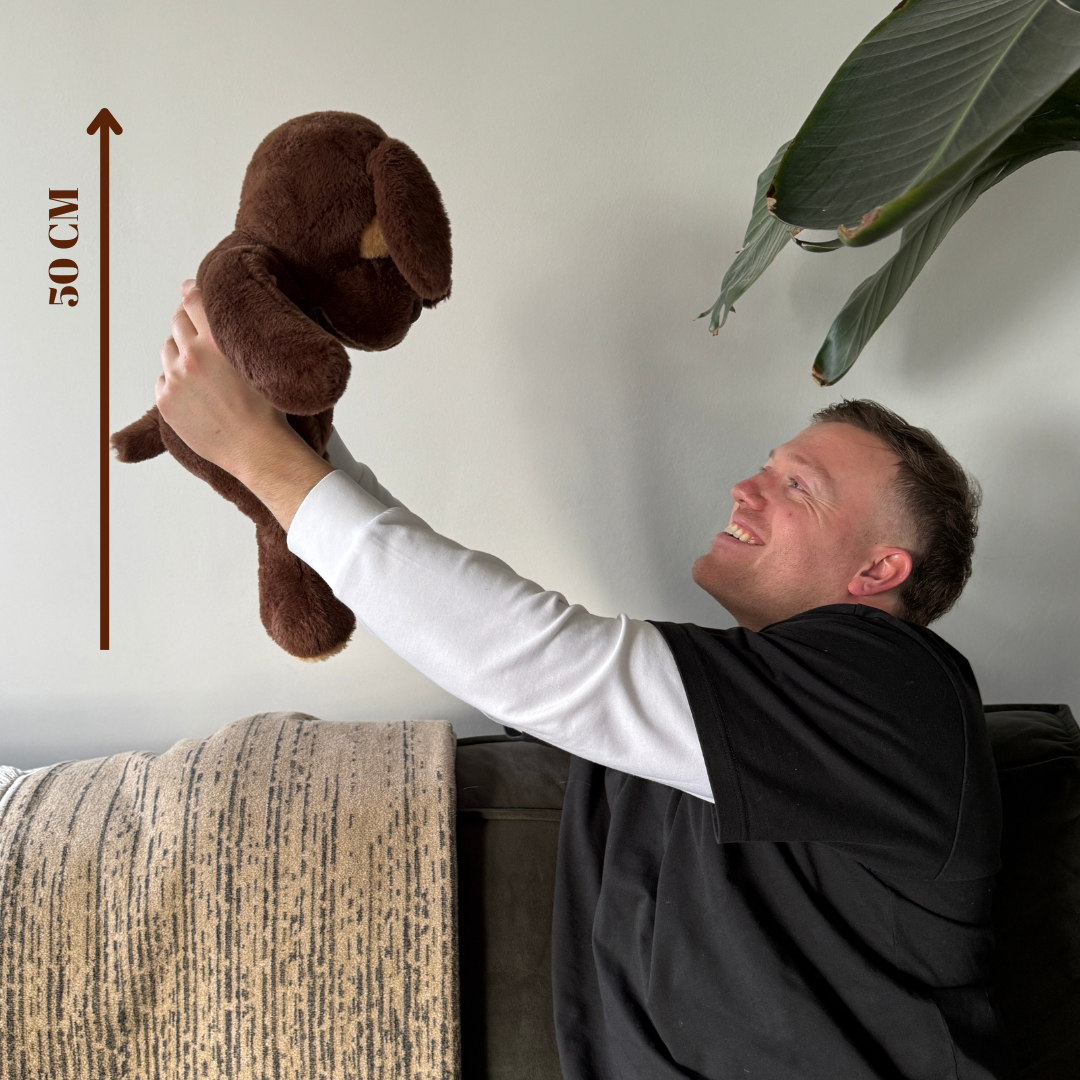 Het Troostmaatje (50 cm) omhoog gehouden om de grootte van de verzwaringsknuffel hond te tonen.
