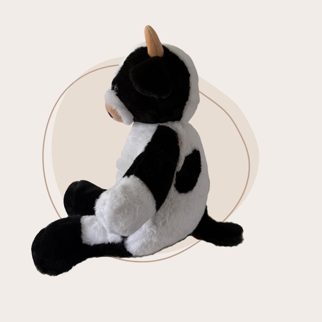 Zijaanzicht van de zittende zwart-witte koe knuffel, tonend de zachte hoorntjes en details.